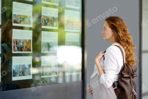 Preview: Young pregnant woman exploring storefront of real estate agency.