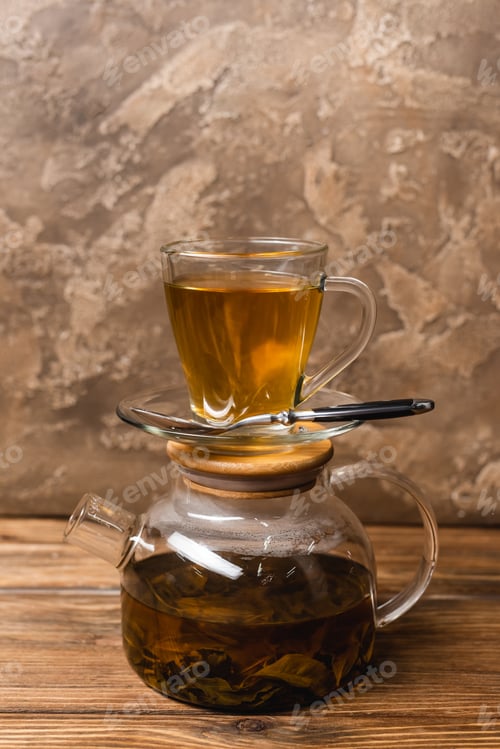 Preview: Cup of tea on glass teapot on wooden surface on textured stone background