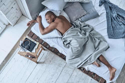 Preview: Totally relaxed. Top view of young African man sleeping while lying in the bed at home
