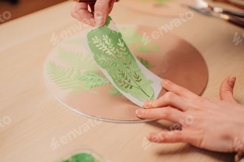 Preview: Artist removing stencil revealing fern design on wooden surface