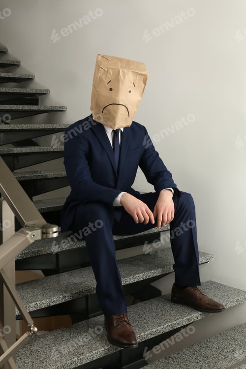Preview: Man wearing paper bag with drawn sad face indoors