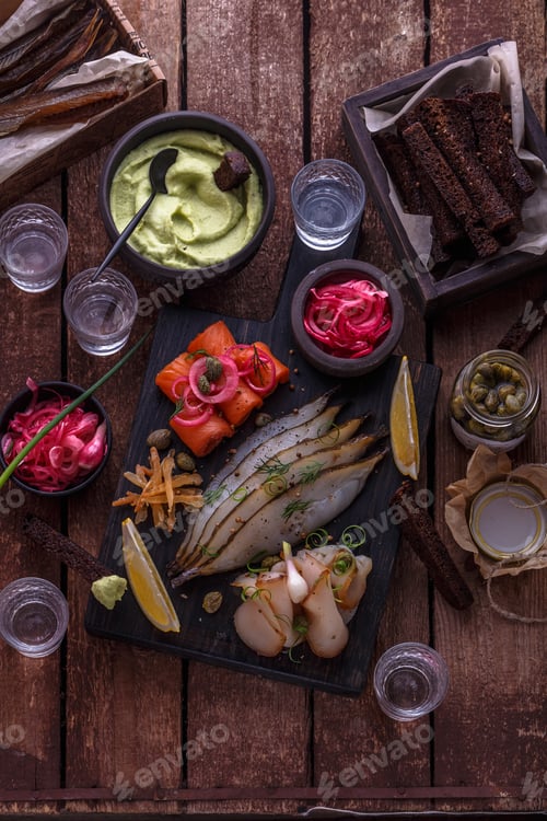 Preview: Assorted marinated fish on dark cutting board with vodka shots.