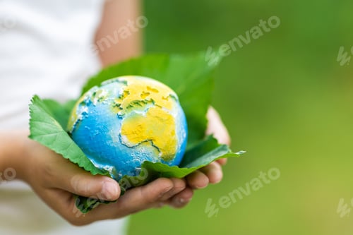 Preview: Kid holding small planet in hands against spring or summer green background. Ecology, environment