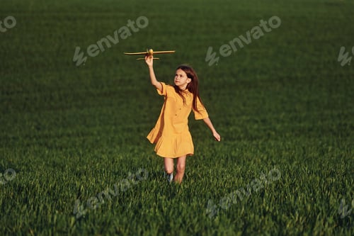 Preview: Running forward with toy plane. Happy girl have a walk outdoors on the field at summer