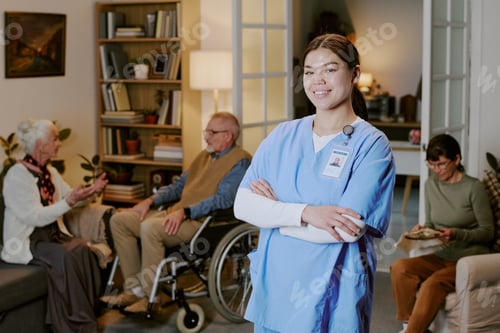 Preview: Young Adult Hispanic Woman Nurse Smiling While Standing in Senior Care Facility