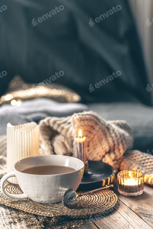 Preview: Cozy home composition with a cup of tea, candles and a knitted element.
