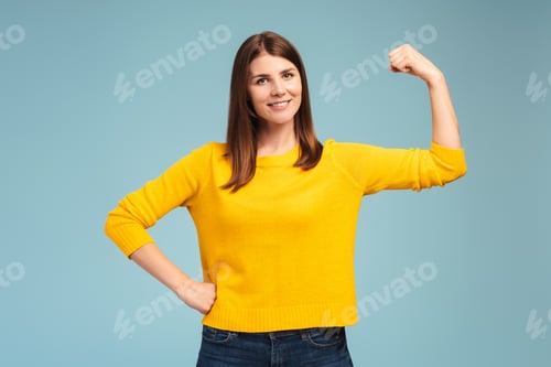 Preview: Cute woman showing her strong arms, biceps, looking at camera standing isolated on blue background