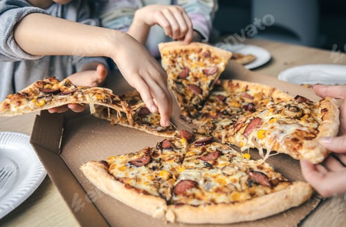 Preview: Young people taking slices of hot pizza from cardboard box at table.