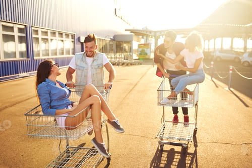 Preview: Group of happy young people having fun on shopping trolleys. Young people racing on shopping cart.