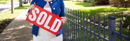 Preview: Female standing on a park road holding a sign with the inscription "Sold"