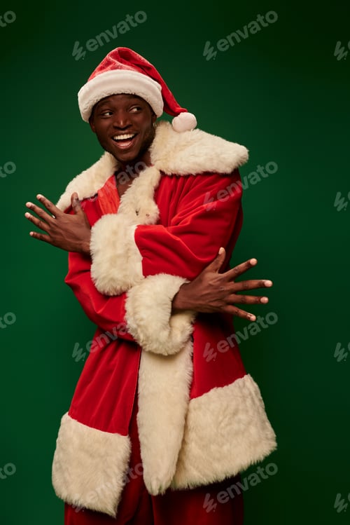 Preview: excited african american man in santa claus costume gesturing and looking away on green backdrop