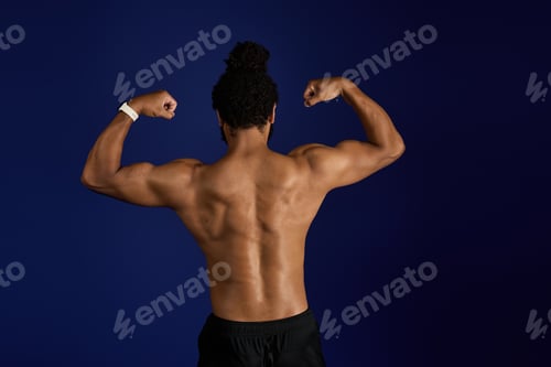 Preview: Sportive black man showcasing strength with a powerful pose against a blue backdrop