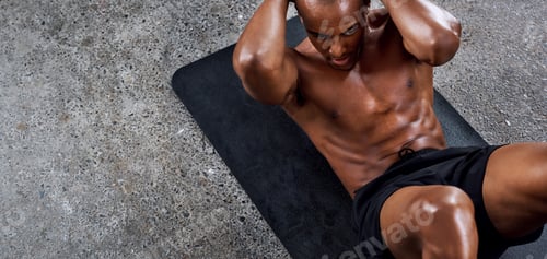 Preview: Shot of a sporty young man doing sit ups as part of his exercise routine