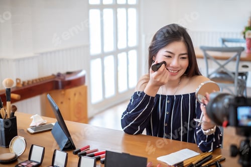 Preview: Asian woman blogger with makeup cosmetics recording video clip by smartphone at home.