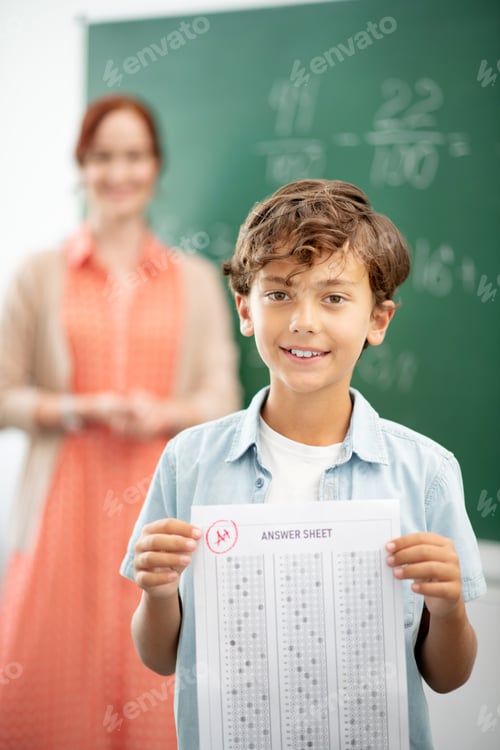 Preview: Dark-haired boy standing near blackboard with answer sheet