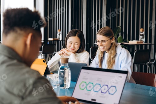 Preview: Coworkers collaborating on project using laptops in modern office