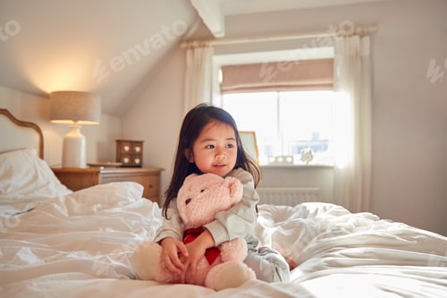 Preview: Young Girl Sitting On Bed Wearing Pyjamas At Home Cuddling Soft Toy