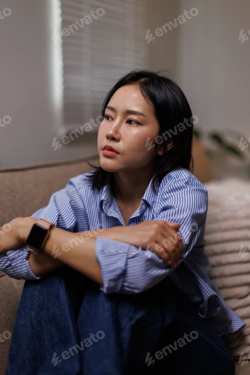 Preview: Young thoughtful woman sitting on a couch, crossing her arms and looking away