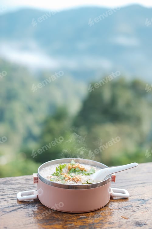 Preview: Pork porridge or rice soup with pork and vegetables on wood table against Mountain View background