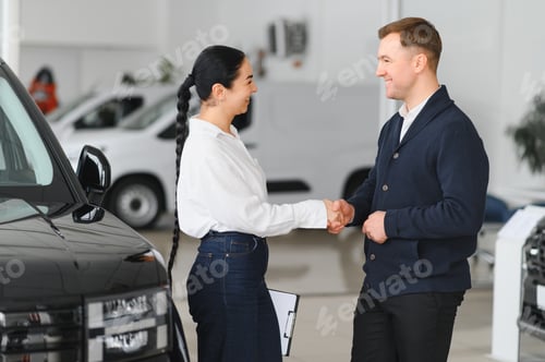 Preview: Friendly female car dealer standing at fancy car showroom and having consultations with a customer