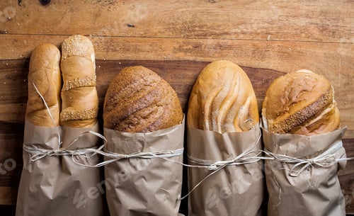 Preview: Different fresh baked bread in paper bags on wooden table.