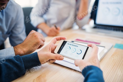 Preview: Group of businesspeople with smartphone working together in office, midsection.