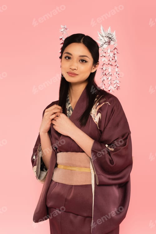 Preview: Pretty japanese woman with kanzashi in hairdo looking at camera isolated on pink