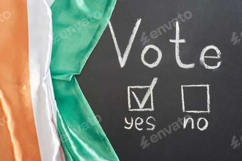 Preview: top view of vote lettering and check mark near yes word on black chalkboard near flag of Ireland