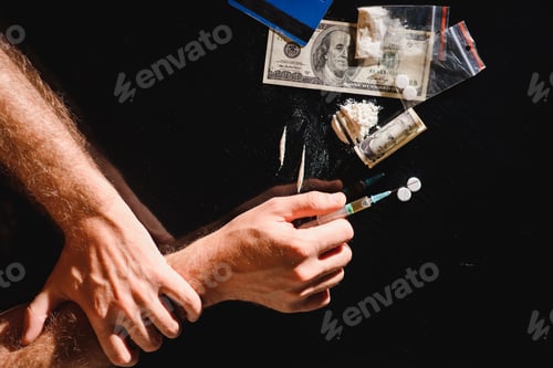 Preview: Man's hands trying to abstain from drugs on dark table with cooked heroine, pills