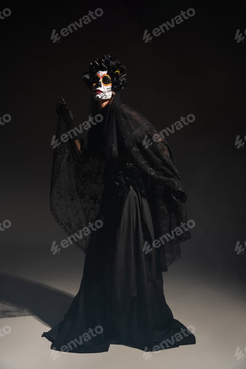 Preview: full length of woman in traditional day of dead costume and catrina makeup posing on black