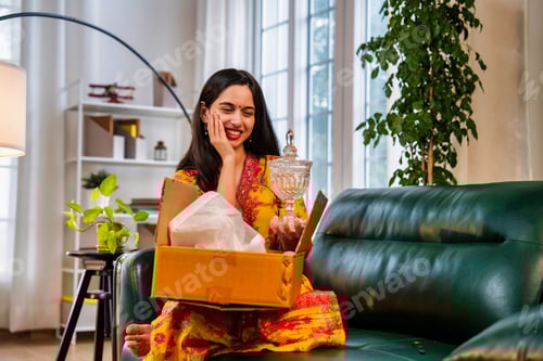 Preview: Happy Indian Asian girl in salwar kameez smiling while unboxing an exciting cardboard parcel