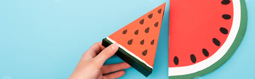 Preview: partial view of female hand with paper watermelon slices on blue background, panoramic shot