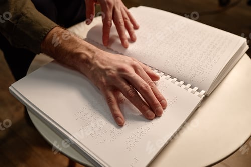 Preview: Middle Aged Man Reading Braille Book with Hands in Library Setting