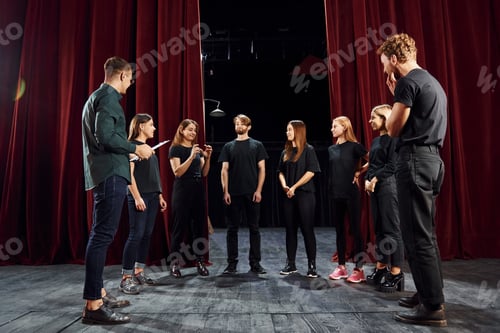 Preview: Working together. Group of actors in dark colored clothes on rehearsal in the theater