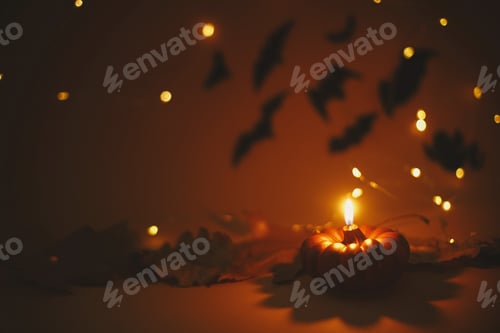 Preview: Happy Halloween. Pumpkin candle burning on dark orange background with lights and flying black bats