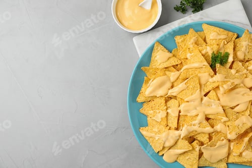 Preview: Plate of Mexican nacho chips with sauce on grey table, flat lay. Space for text