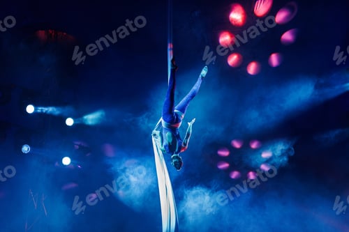 Preview: Aerialist performs a dangerous trick on a fabric high under dome of the circus under the spotlight.