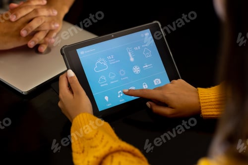 Preview: Hands of diverse couple at home, woman using tablet with smart home interface on screen