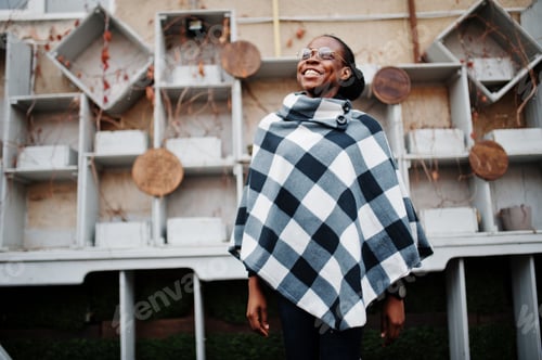 Preview: African woman in checkered cape and eyeglasses posed outdoor.