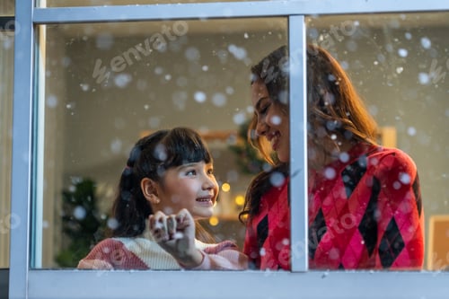 Preview: Adorable child looking at the window and admire snowflakes with mother.