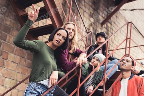 Preview: group of young stylish people pointing and looking away on stairs of industrial building
