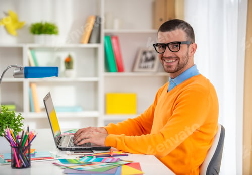 Preview: Smiling creative professional working on laptop in office.