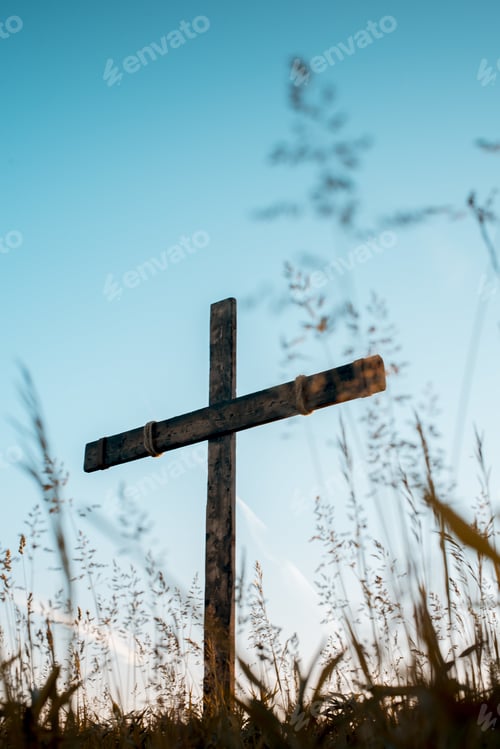 Preview: Low angle vertical shot of a hand made wooden cross in a grassy field with a blue sky in background