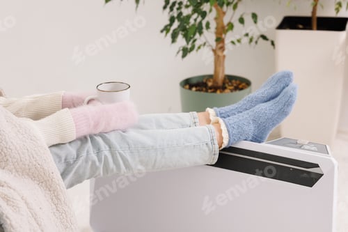 Preview: Young girl in warm clothes and with a cup of tea at home. Heating season concept
