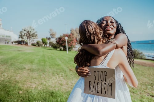 Preview: Two women hug each other in a park while holding the sign "Stop Racism".