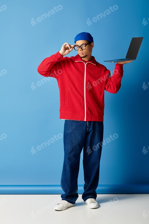 Preview: Stylish young man in beanie showcases his trendy look against a vibrant blue backdrop