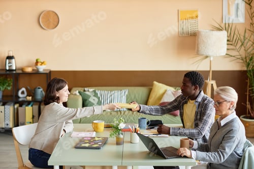 Preview: Male African American Office Worker Passing Colleague Book at Meeting Table Indoors