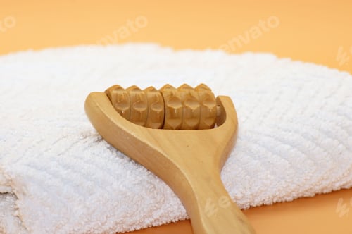 Preview: Wooden massage roller placed on a white towel with an orange background