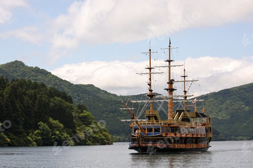 Preview: Wide angle shot of a ship sailing in front of a mountain covered in trees and plants