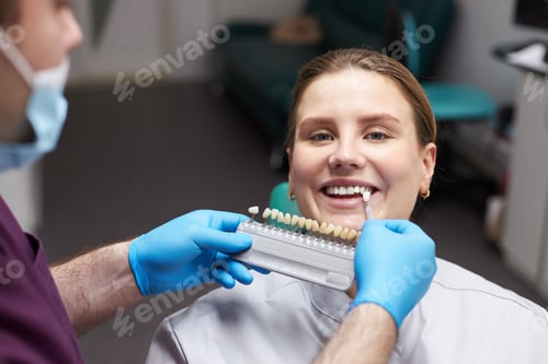 Preview: Close-up female patient looking at camera while orthodontist, choosing the shade of dental veneers